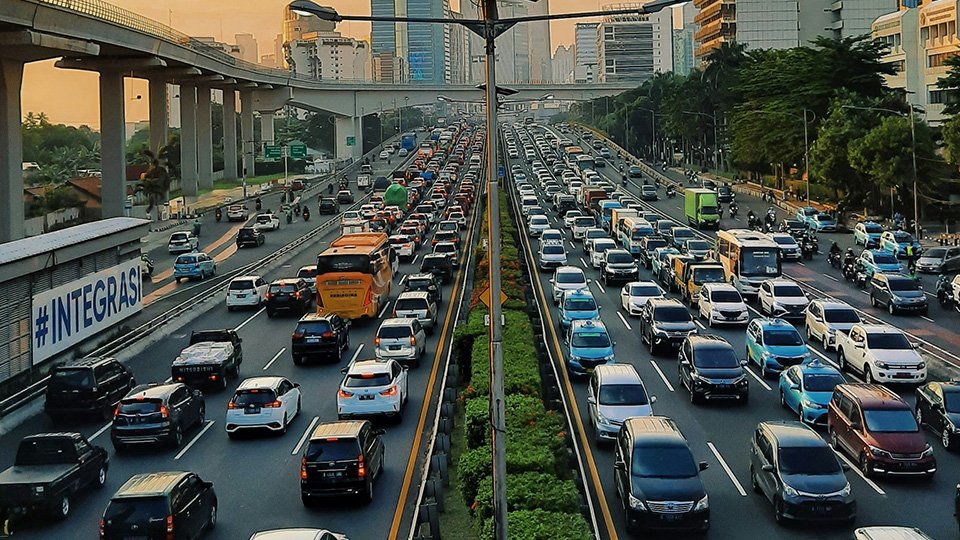 A Imagem mostra vias cheias de veículos, em horário de pico de trânsito em meio à cidade.