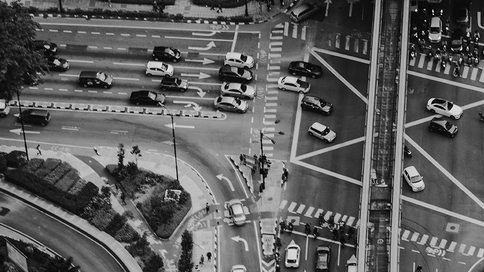 A Imagem mostra um cruzamento em preto e branco, com veículos como carros passando.