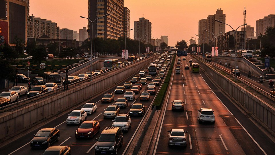 A imagem mostra o fim de tarde numa cidade com ruas movimentadas , com diversos veículos passando