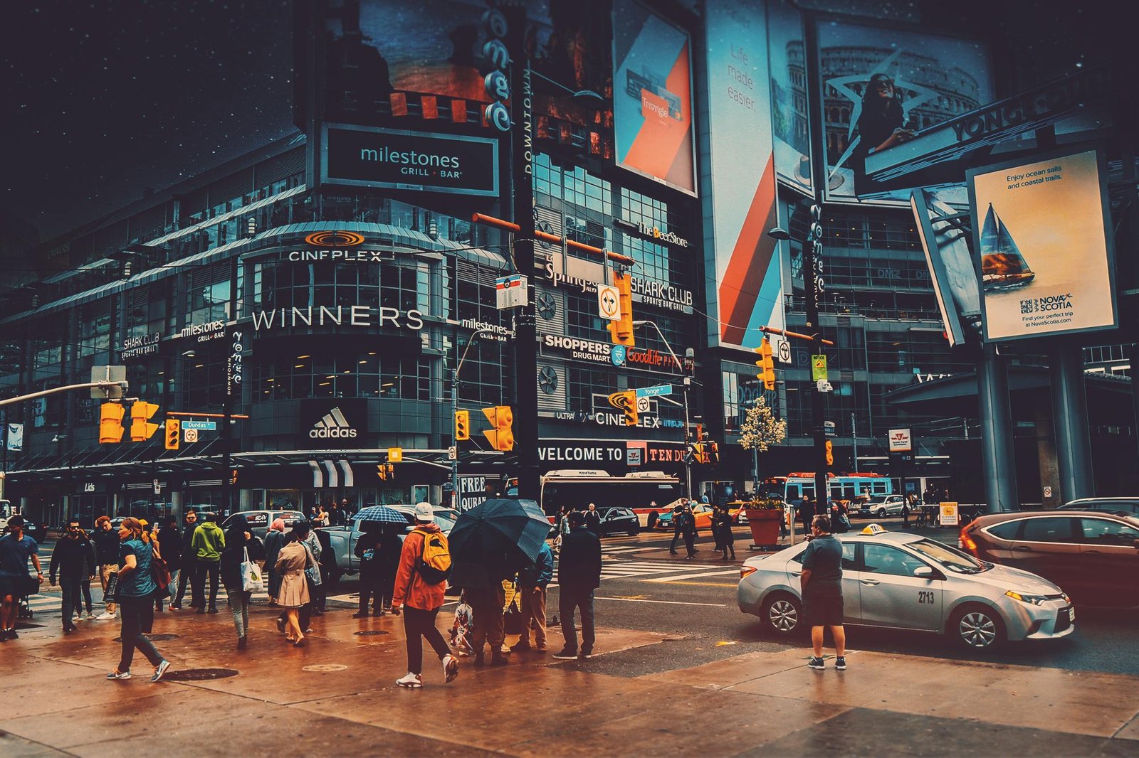 Imagem de uma rua, com vista para carros, pedestres, painéis digitais de anúncios