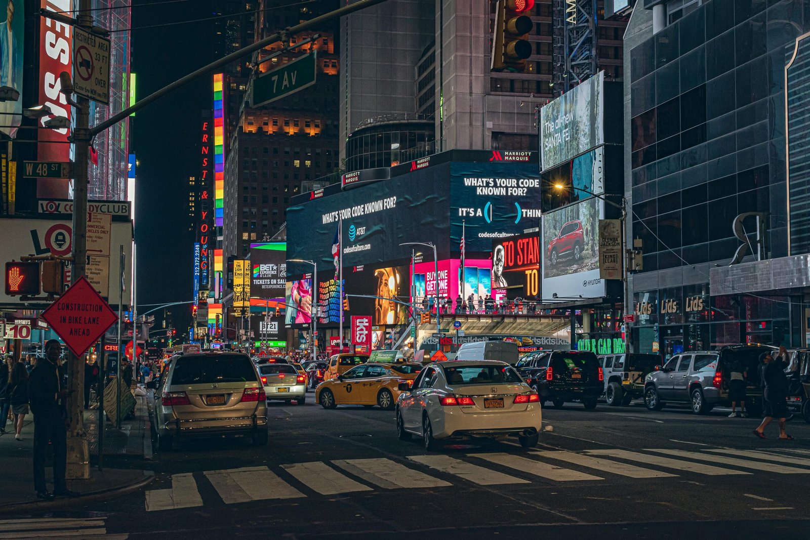 Rua com veículos, perto de centro comercial com diversas propagandas de paineis digitais, como centro comercial