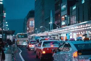 A imagem mostra uma avenida principal movimentada por veículos de noite