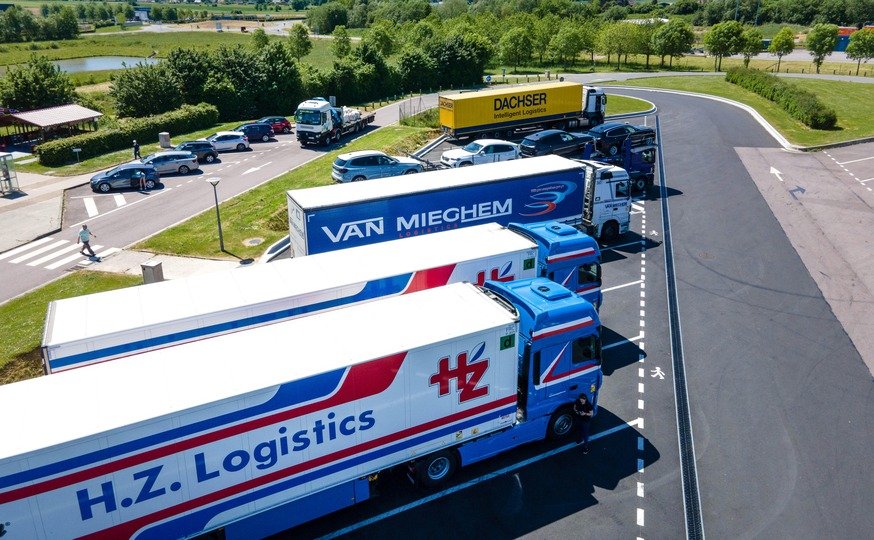 A Imagem mostra vários caminhões de logística e manufatura, estacionados em fileira, num pequeno estacionamento!